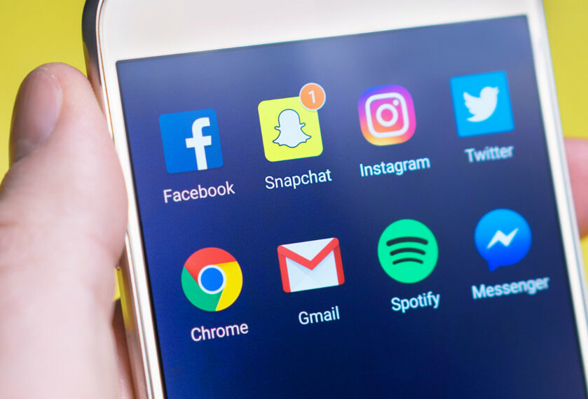 En hand håller i en mobiltelefon där skärmen visar olika sociala medier-applikationer