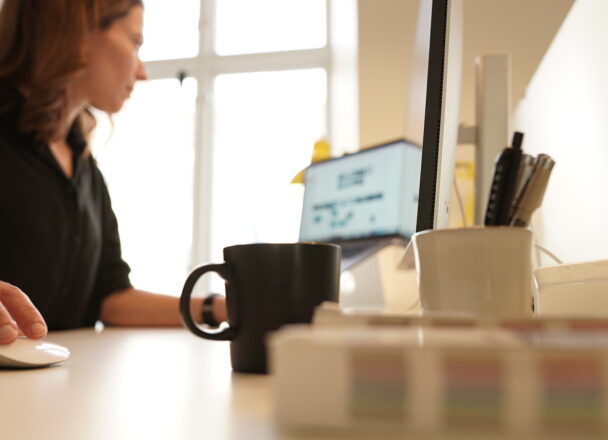 En kvinna sitter framför en datorskärm med en kaffekopp i förgrunden.