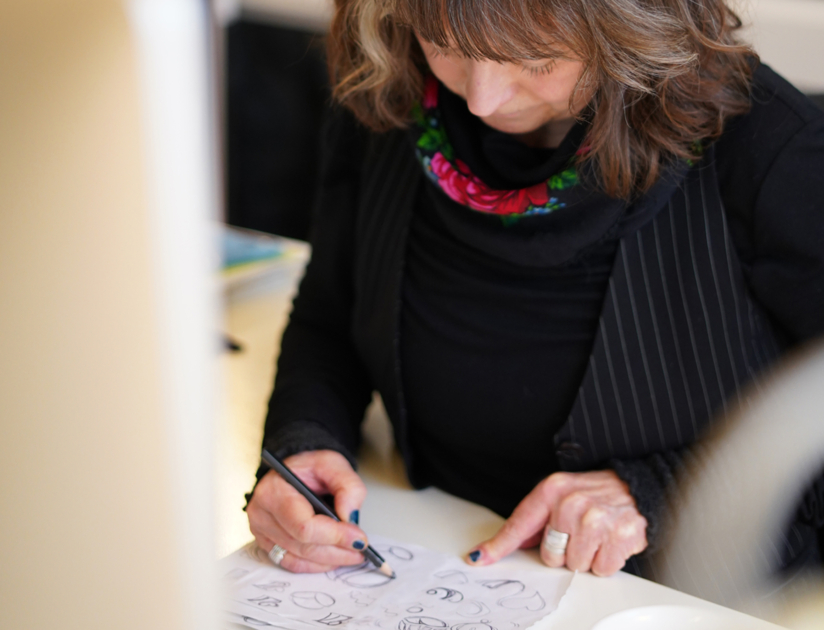Grafisk designer Catarina Malm vid ett skrivbord, skissandes under logotypprocessen.