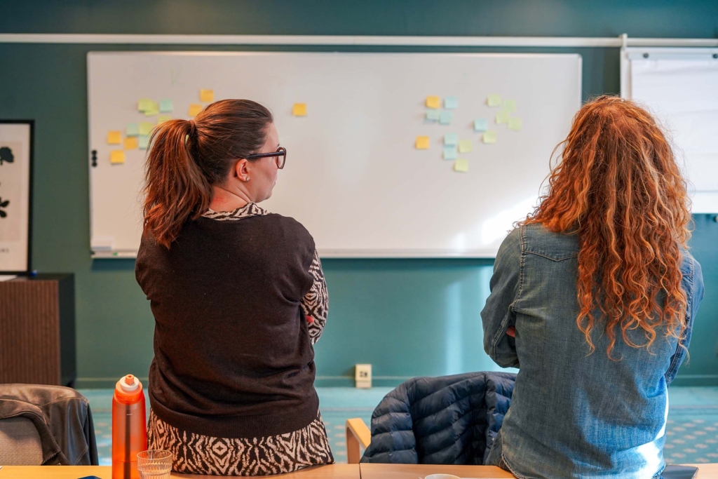 Kommunikations- & varumärkesstrateg Hanna Flink och Content Designer Frank Kooistra tittar på en whiteboard full med post it lappar under en workshop i kreativitet.